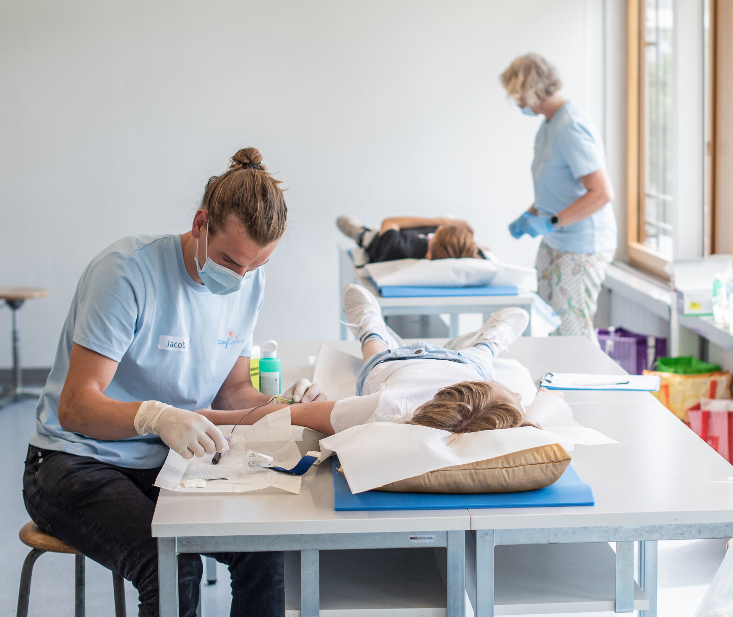 Ciao-Corona team takes blood from the test persons. Several students can be supervised at the same time. The blood collection takes place in gymnasiums, singing halls or other suitable premises of the schools